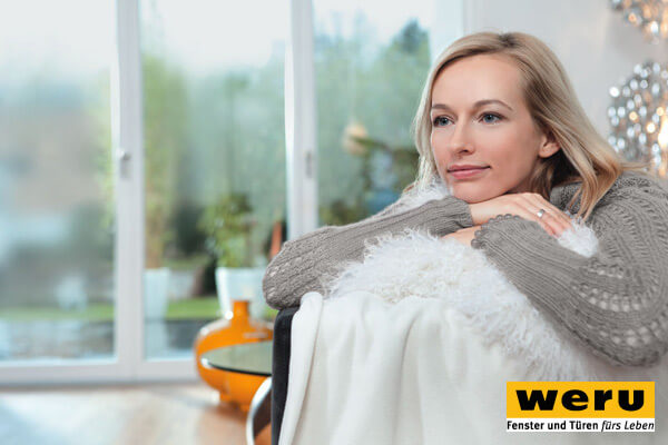 Frau entspannt auf der Couch, hinter ihr eine breite Fensterfront